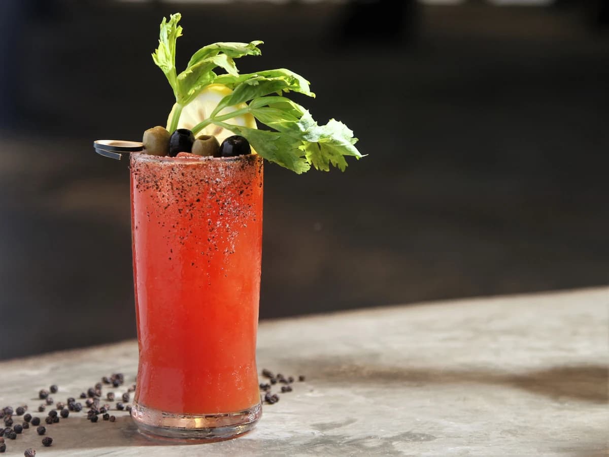 A Bloody Mary in a highball glass garnished with a celery stalk and lemon wedge