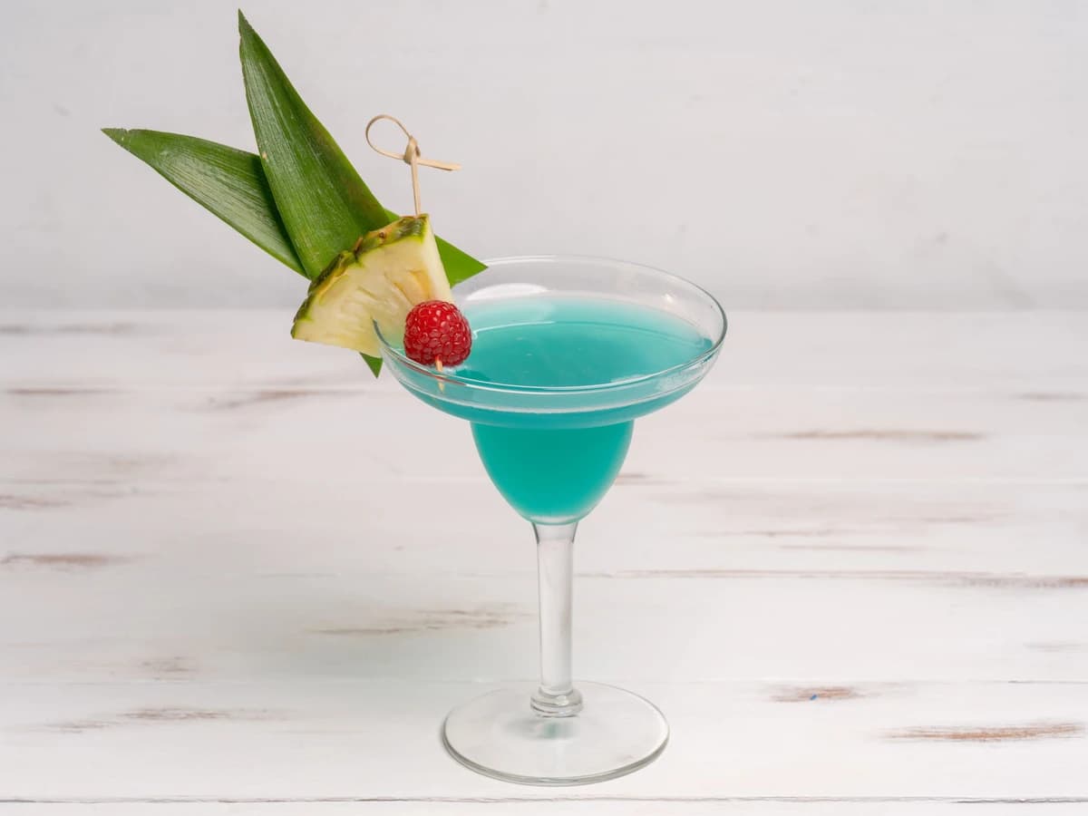 A bright blue Blue Hawaiian cocktail blended and served in a hurricane glass with a pineapple wedge