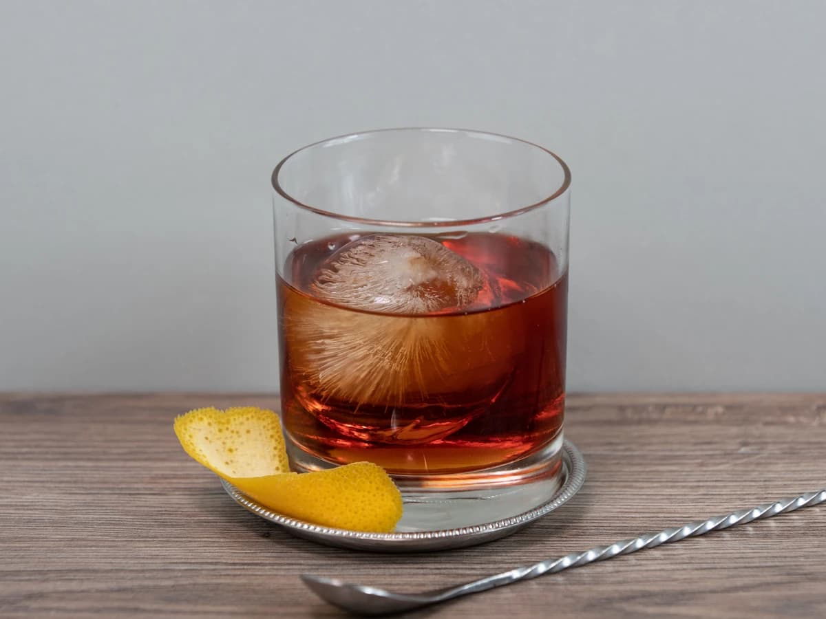 A Boulevardier in a rocks glass with a large ice cube and orange peel