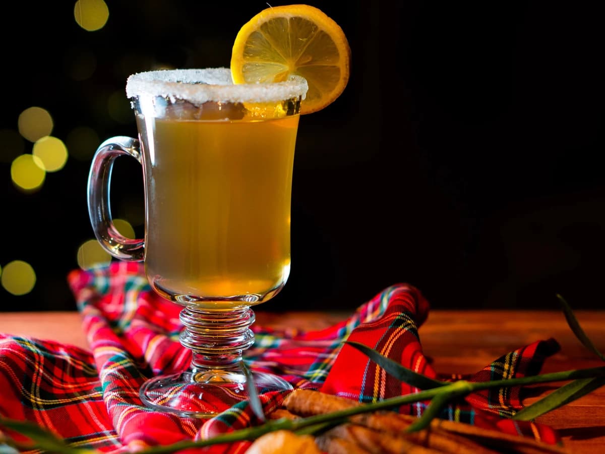 A Hot Toddy in a glass mug with a clove-studded lemon wheel and steam rising