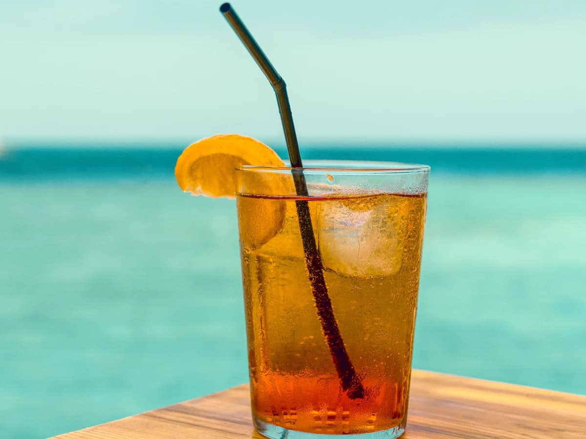 A Long Island Iced Tea in a tall highball glass, dark amber with a lemon wedge