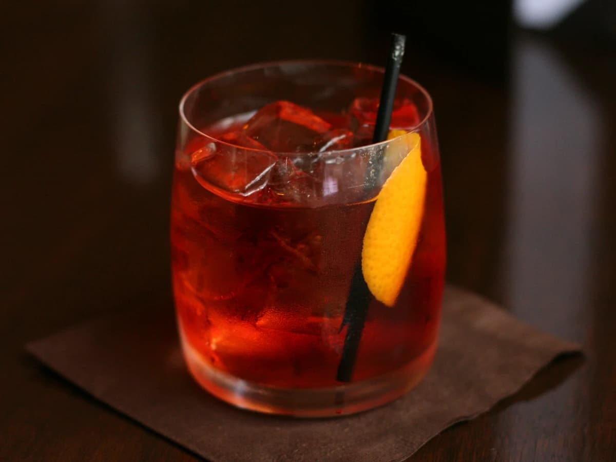 A Negroni in a rocks glass with a large ice cube and orange peel