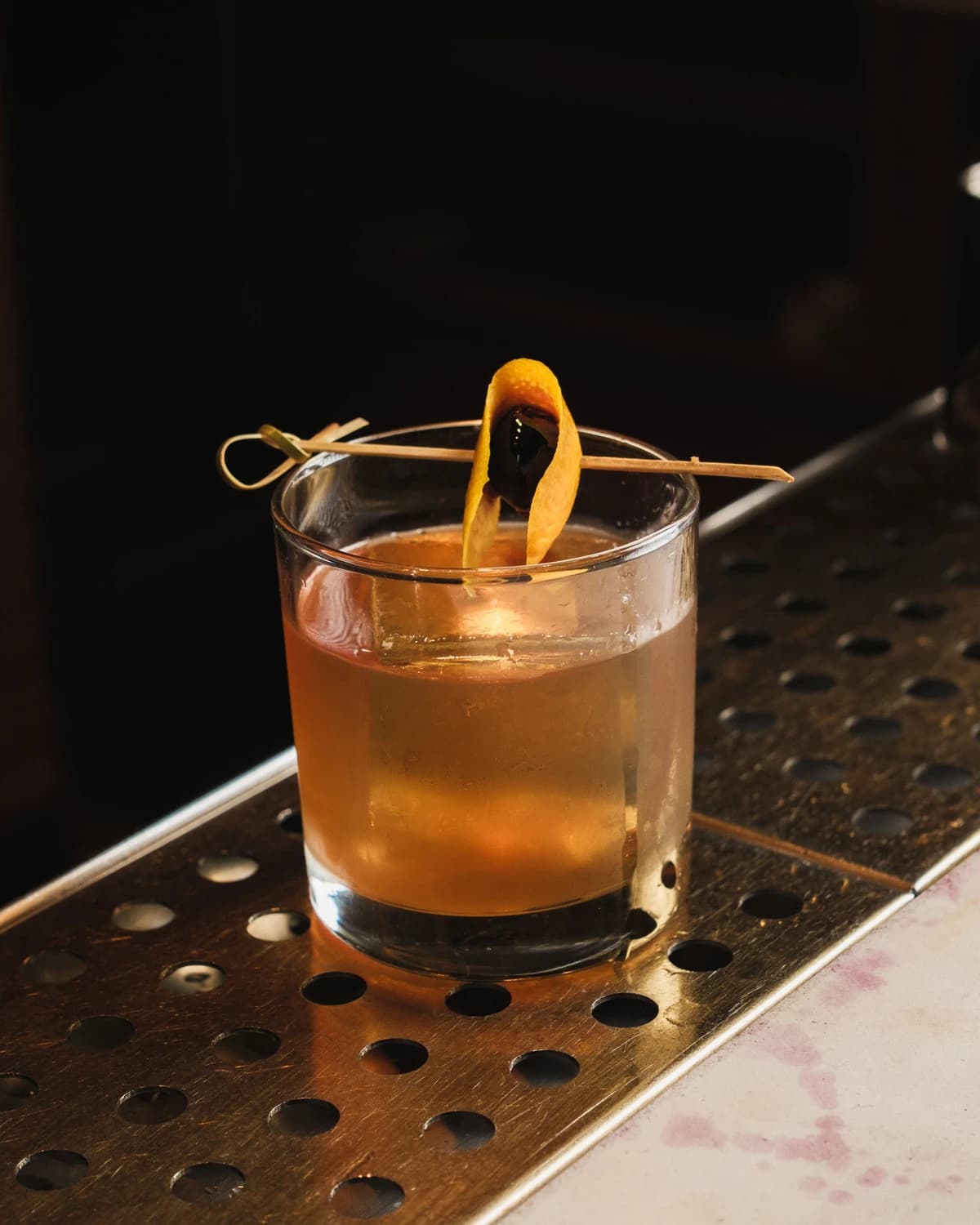 An Old Fashioned in a rocks glass with a large ice cube and orange peel