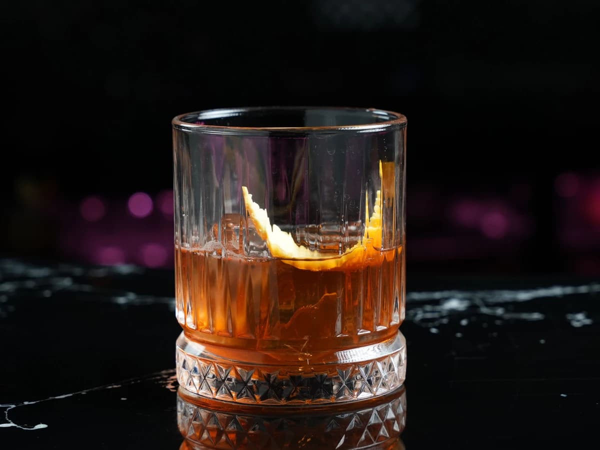A Sazerac in a rocks glass with a lemon peel expressed over the top, no ice