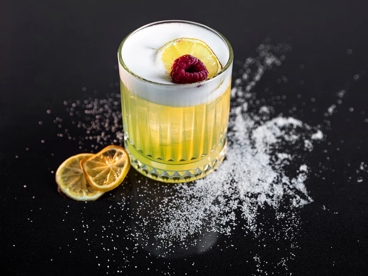 A Whiskey Sour in a rocks glass with a silky white foam and a lemon wheel